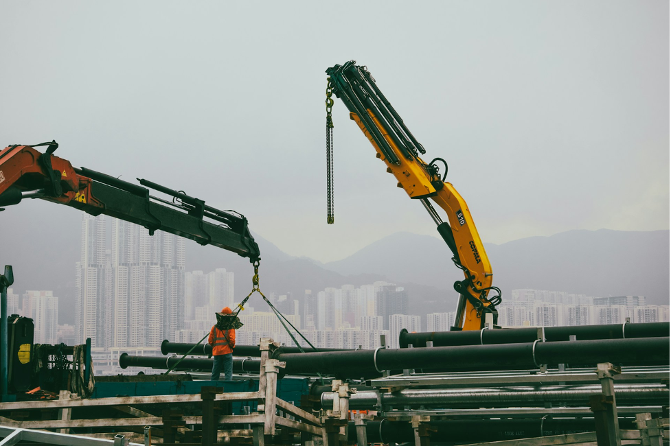 Two cranes lifting up pipes at a construction site