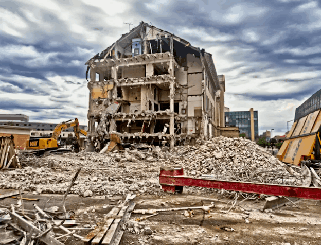 Partially demolished commercial building with construction debris and excavator